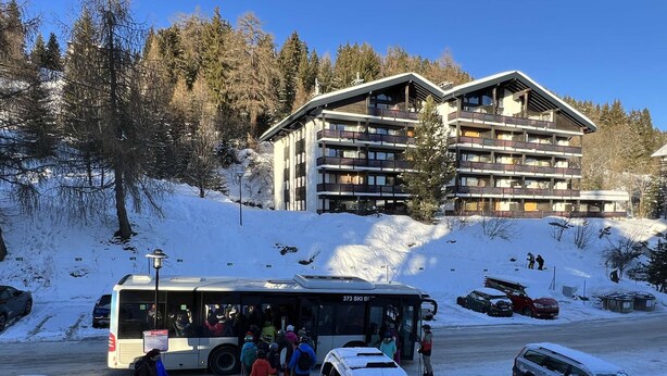 A ski resort with a bus, people with skis, and a building with multiple balconies. - cosy 26 sqm studio is located in the Swiss Alps ski resort of Les Collons (Vex (Les Collons))