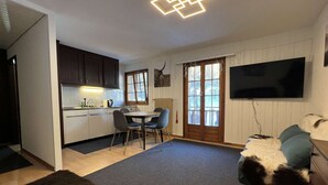 A modern kitchen with dark cabinets, a white refrigerator, and a dining area with a table and chairs. - cosy 26 sqm studio is located in the Swiss Alps ski resort of Les Collons (Vex (Les Collons))