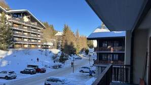A snowy mountain road with parked cars, a building with balconies, and a clear blue sky. - cosy 26 sqm studio is located in the Swiss Alps ski resort of Les Collons (Vex (Les Collons))