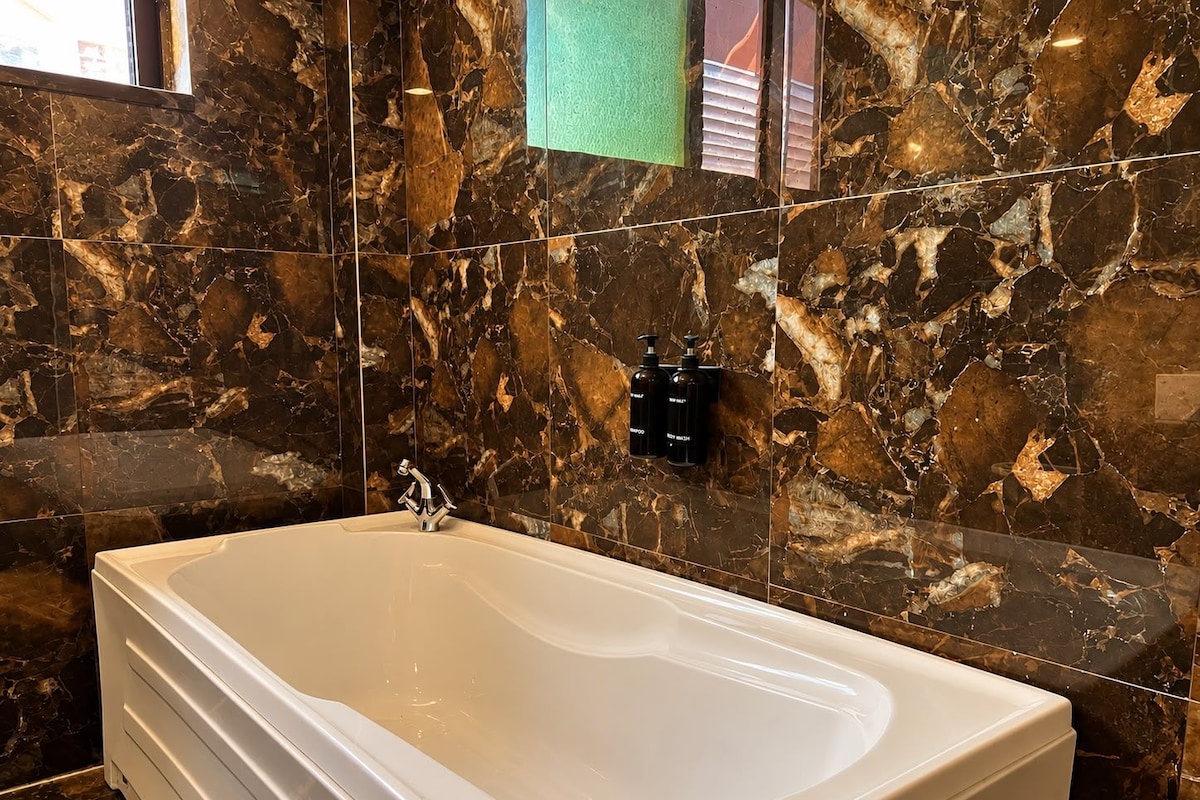 A bathroom with a large bathtub, marble walls, and two bottles of shampoo on the wall.