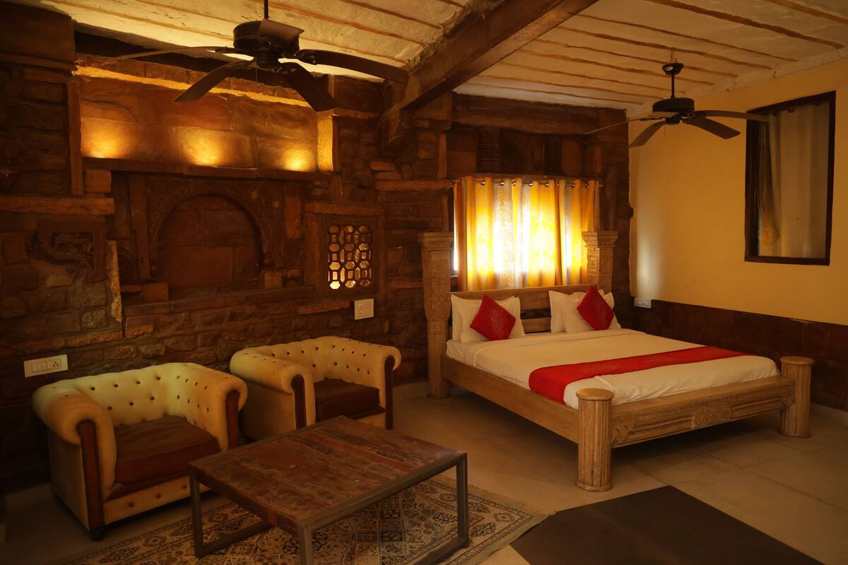 A cozy room with a wooden bed, two armchairs, a small table, and a ceiling fan.