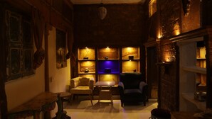 A dimly lit room with a wooden interior, a table, two chairs, and shelves with various items. - Jhankar Haveli (Jodhpur)