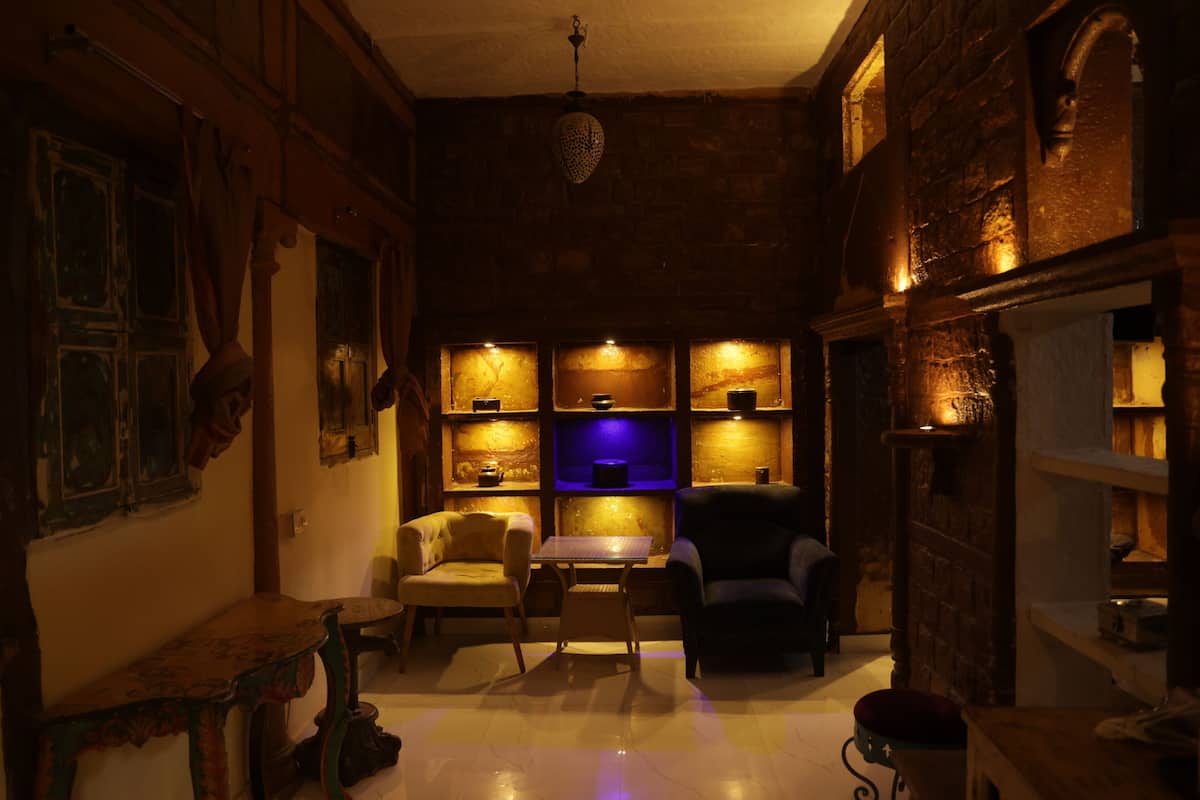 A dimly lit room with a wooden interior, a table, two chairs, and shelves with various items.