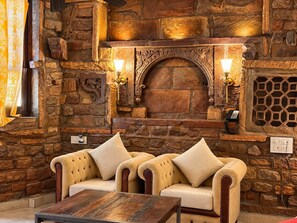 A stone fireplace with two wall-mounted lamps, a cushioned sofa with a wooden coffee table, and a decorative wall panel. - Jhankar Haveli (Jodhpur)