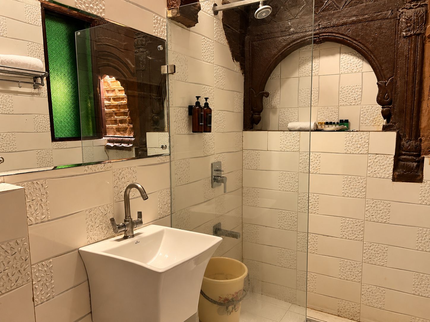 Un baño con lavamanos blanco, cabina de ducha de vidrio y un espejo decorativo.