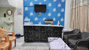 A reception area with a marble counter, a television mounted on the wall, and a check-out time sign. - Yash Paying Guest House (Varanasi)
