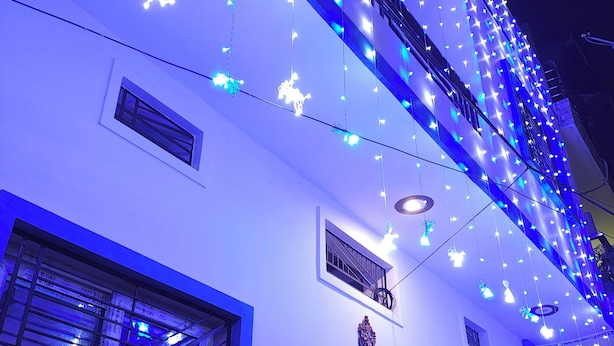 A building facade with multiple windows, some with metal grilles, and decorative lights strung across the upper part of the building. - Yash Paying Guest House (Varanasi)