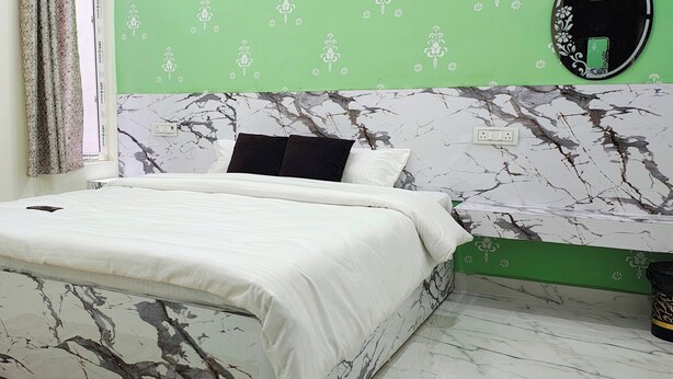 A bedroom with a bed, a green wall, a marble-patterned headboard, and a black trash bin. - Yash Paying Guest House (Varanasi)