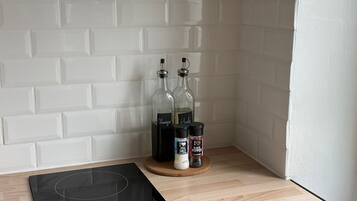Una cocina con baldosas blancas tipo metro, una placa de inducción negra y dos botellas de vino sobre una tabla de madera.