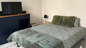 Une chambre à coucher avec un lit, un téléviseur posé sur un bureau en bois, une horloge murale et des œuvres d’art décoratives accrochées au mur.