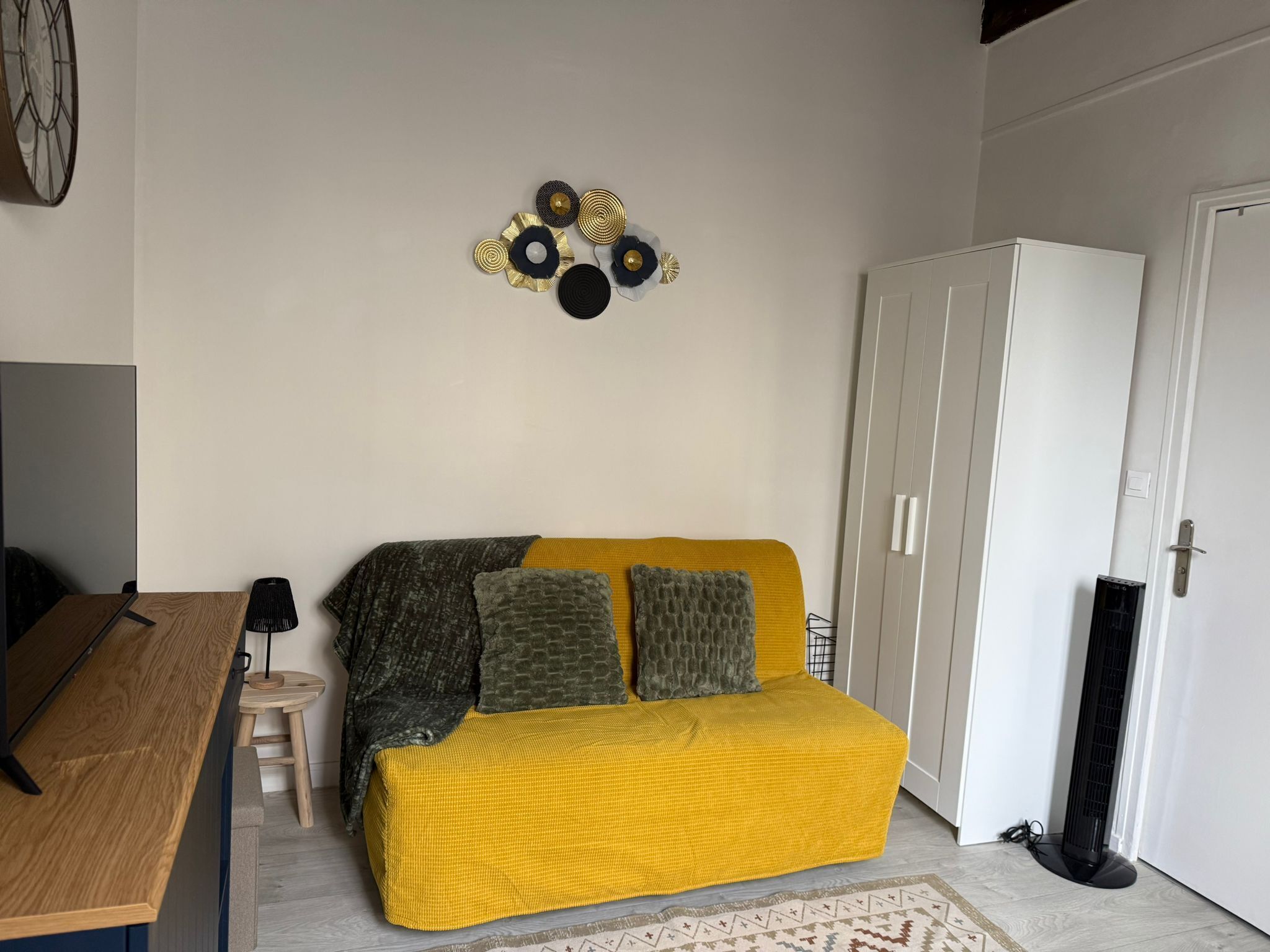 Et værelse med en gul sofa, et lille træbord, en hvid garderobe og en dekorativ vægdekoration.