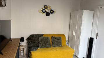 Et værelse med en gul sofa, et lille træbord, en hvid garderobe og en dekorativ vægdekoration.