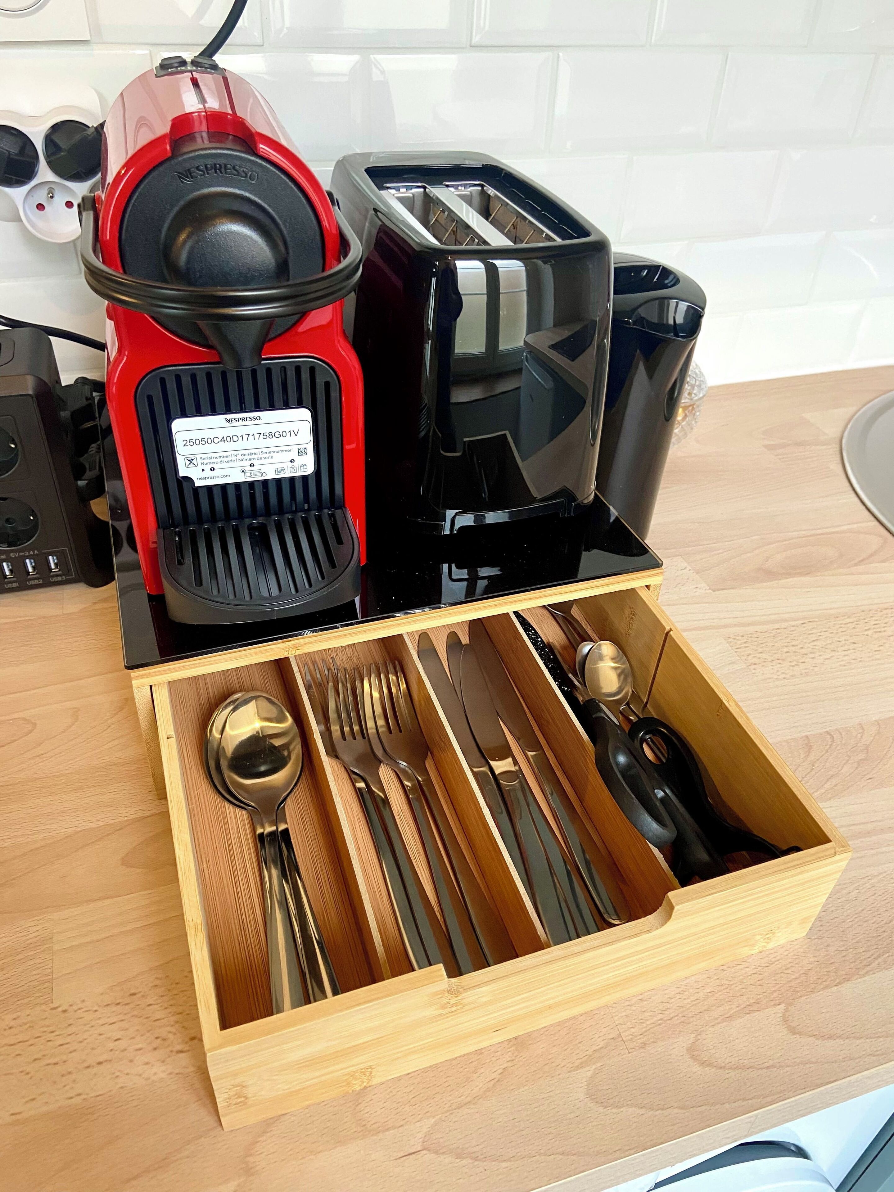 Een keuken met een rode en zwarte espresso machine, een broodrooster en een lade met bestek.