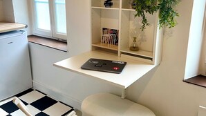 Une pièce de taille modeste, avec un bureau blanc, un ordinateur portable, une petite plante en pot et un sol à carreaux.