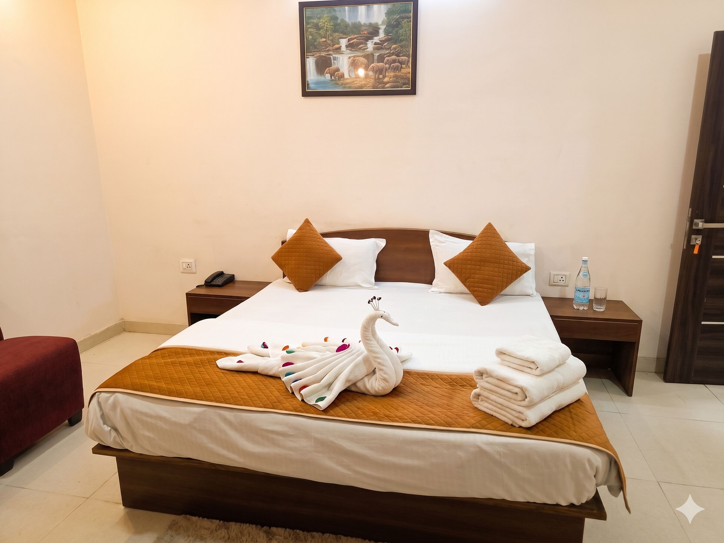 A hotel room with a bed, pillows, a nightstand, a water bottle, and a framed picture on the wall.