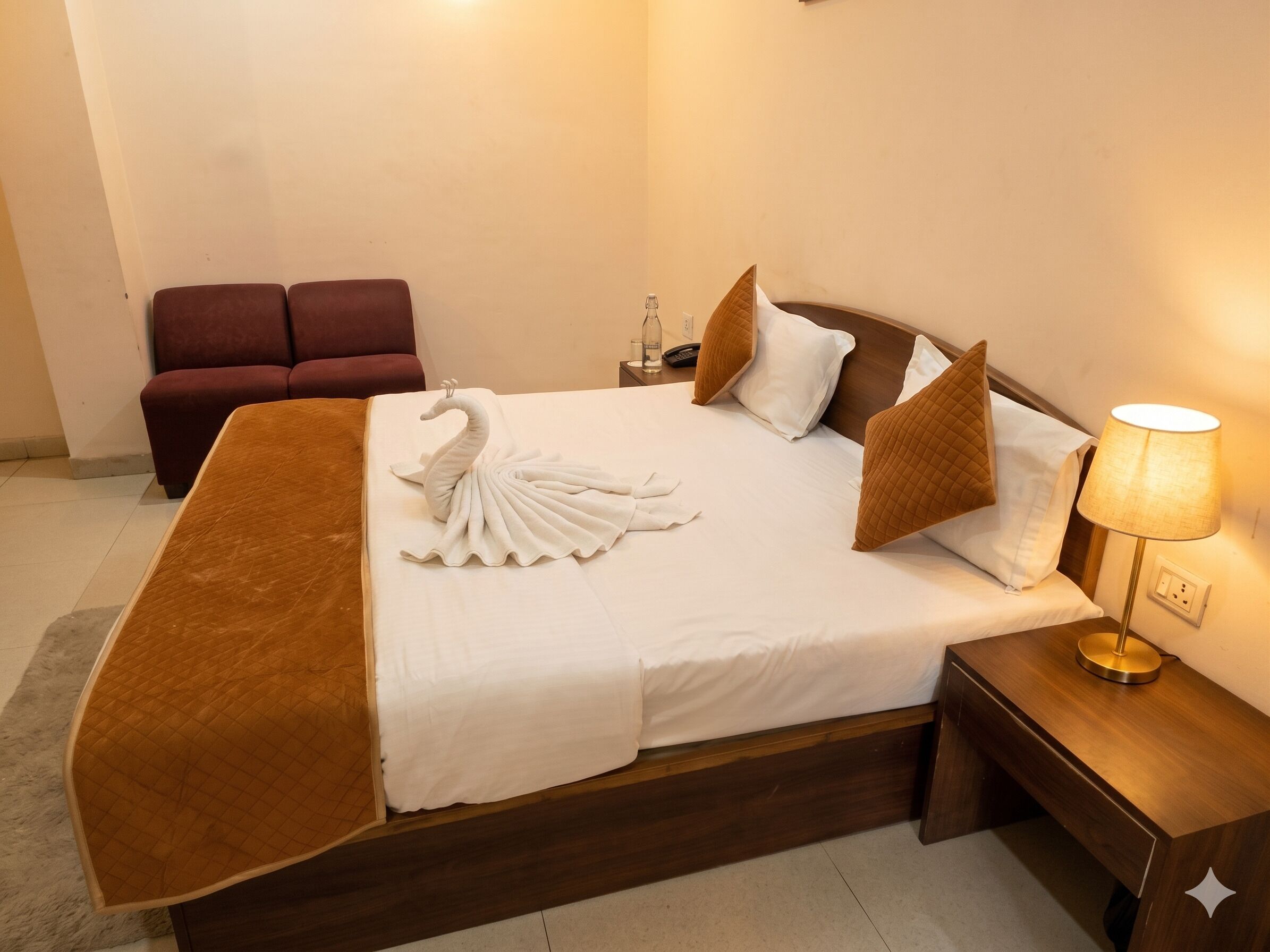 A hotel room with a bed, a nightstand with a lamp, a red sofa, and a swan-shaped towel.
