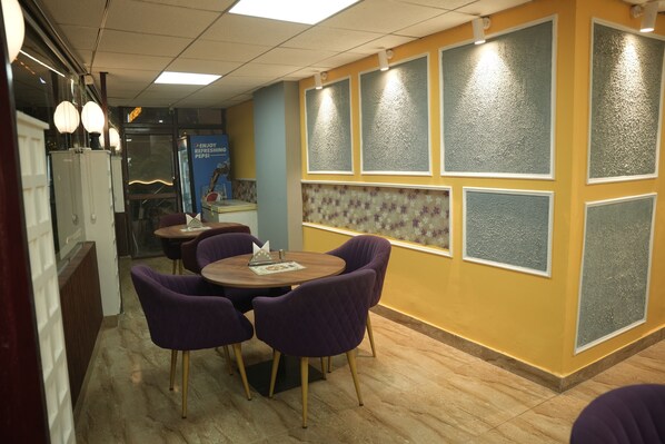Un restaurante con sillas moradas, una mesa de madera y una pared amarilla con paneles de vidrio satinado.