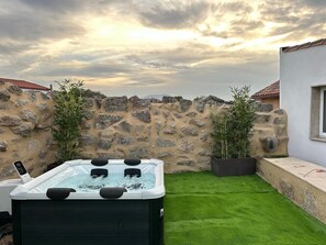 A hot tub in a backyard with a stone wall and green artificial grass.