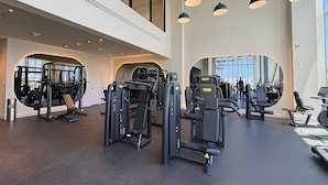 A modern gym with various exercise machines, large windows, and pendant lighting. - Luxury Beachside Oasis (Miami Beach)