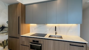 A modern kitchen with wooden cabinets, a black countertop, a built-in oven, and a sink. - Luxury Beachside Oasis (Miami Beach)