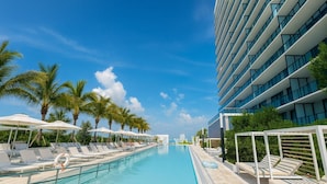 A modern hotel with a poolside area, lounge chairs, and palm trees. - Luxury Beachside Oasis (Miami Beach)