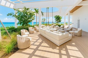 Zona relax esterna e luminosa con un ampio divano bianco, diverse poltrone e vista sull'oceano.