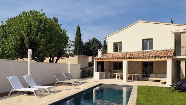 A swimming pool with lounge chairs, a covered outdoor kitchen, and a stone facade house.