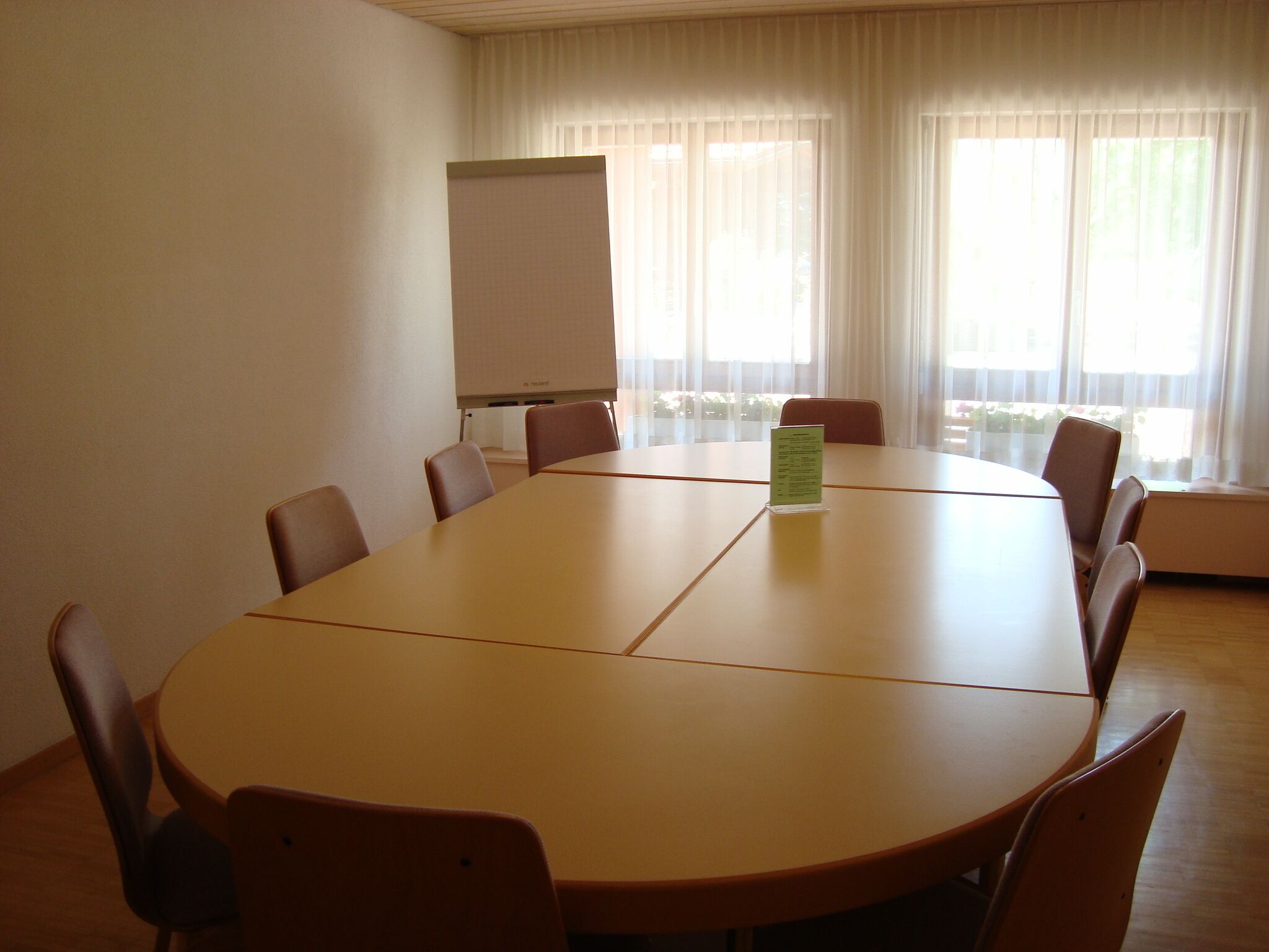 Een vergaderzaal met een grote tafel, stoelen, een whiteboard en een raam met gordijnen.