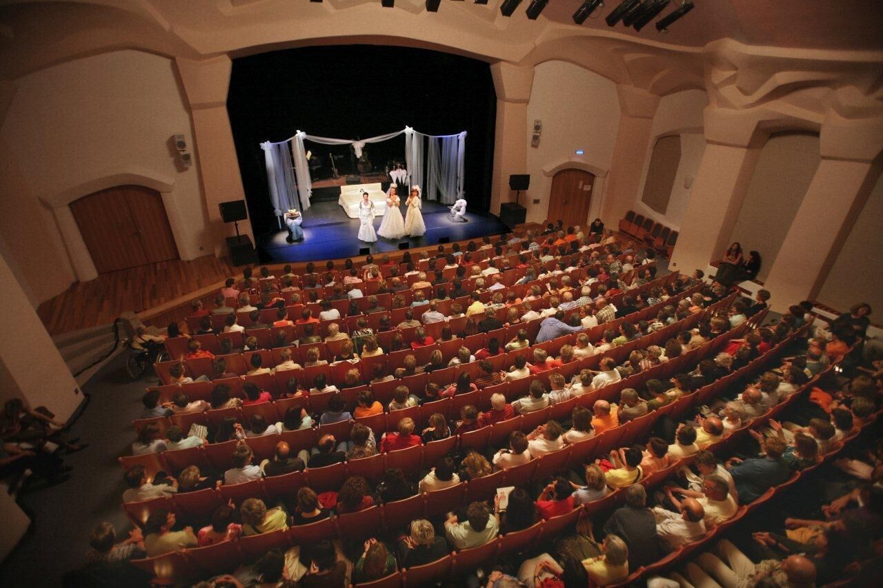 Un auditorio con hileras de asientos rojos y un escenario al frente.