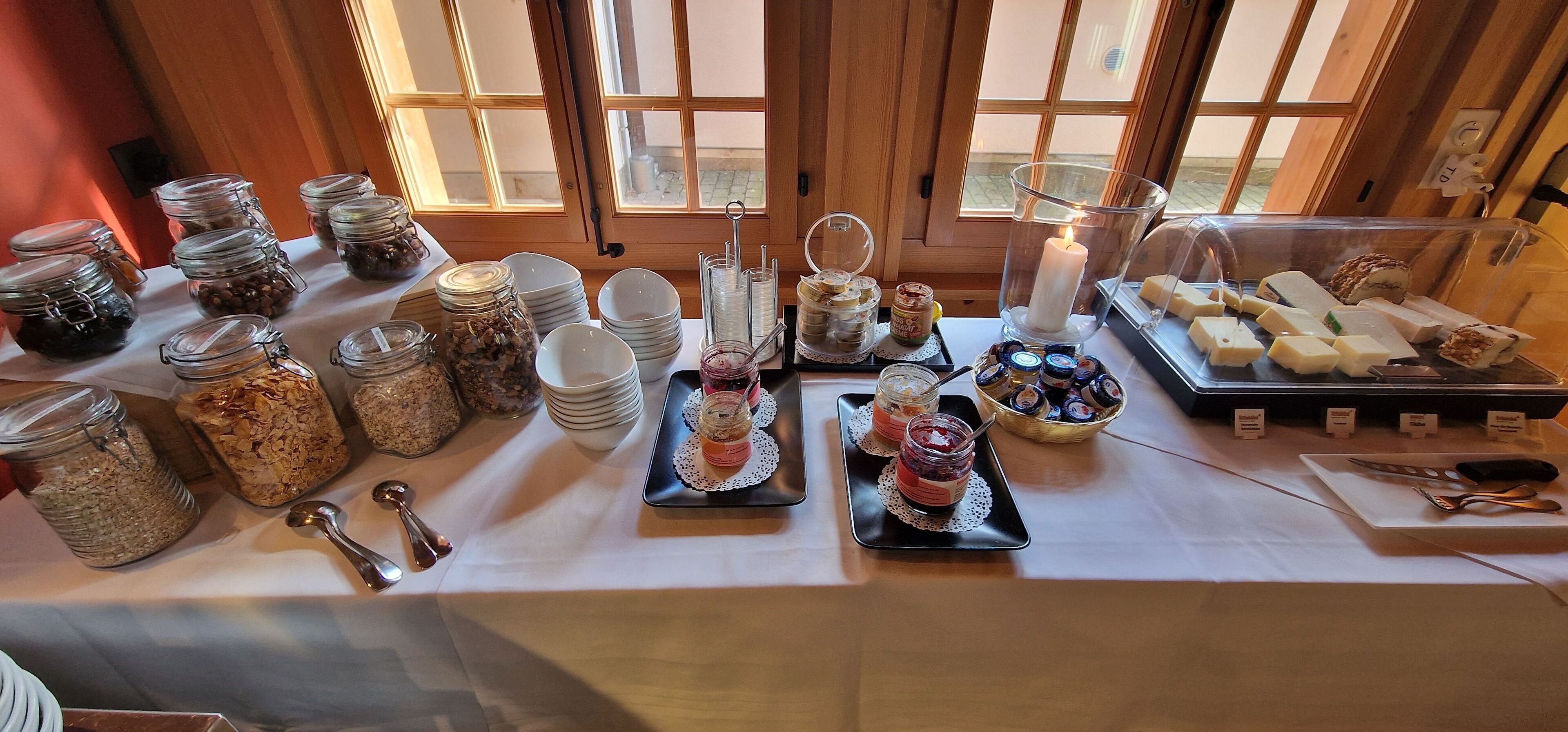 A buffet table with various food items, including jars of preserves, plates, and a candle centerpiece.