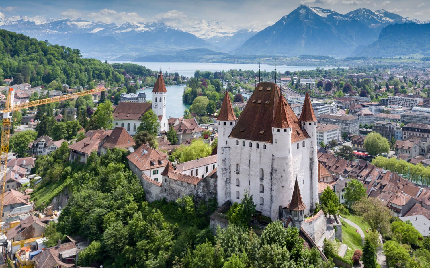 A historic castle with multiple towers, surrounded by lush greenery and a lake.
