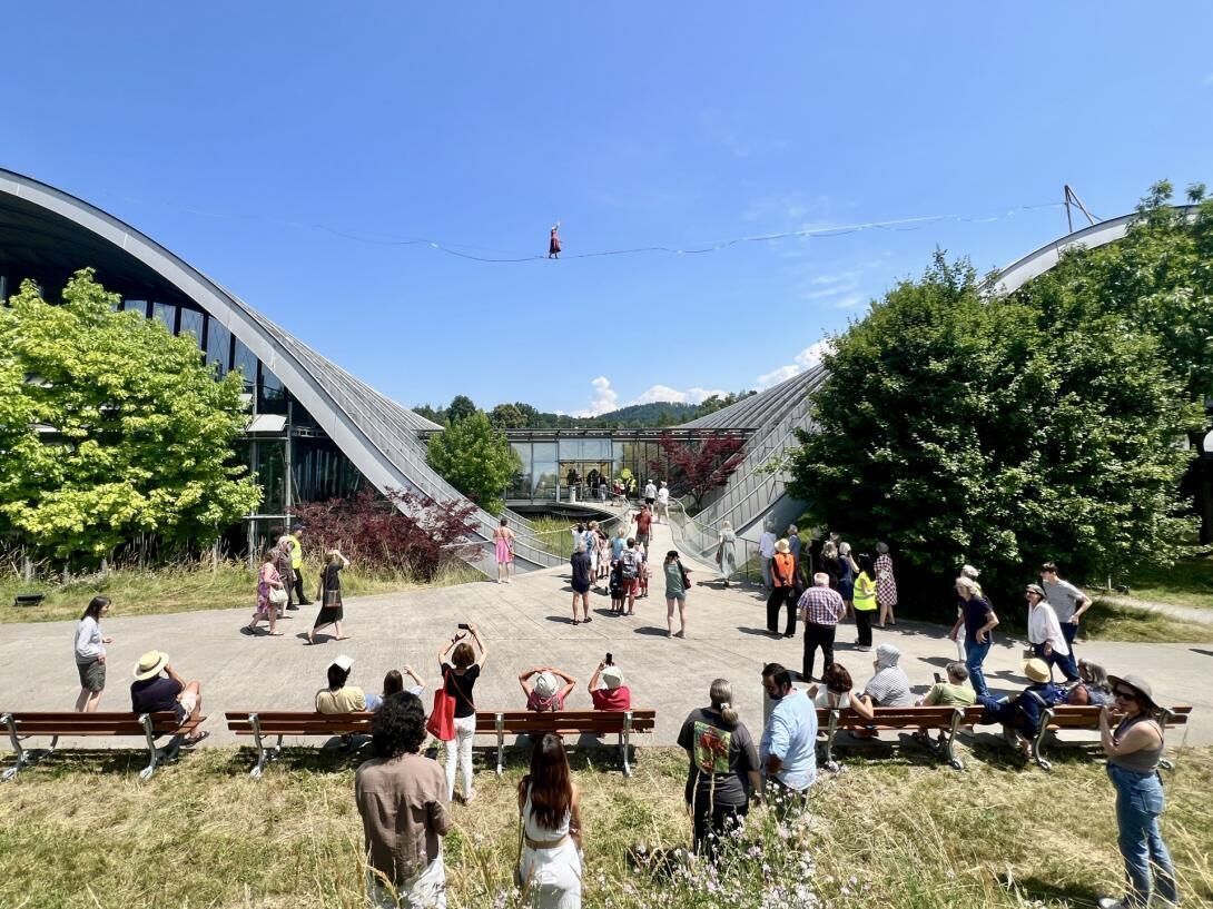 A group of people gathered in an outdoor area with benches and a modern building structure in the background.