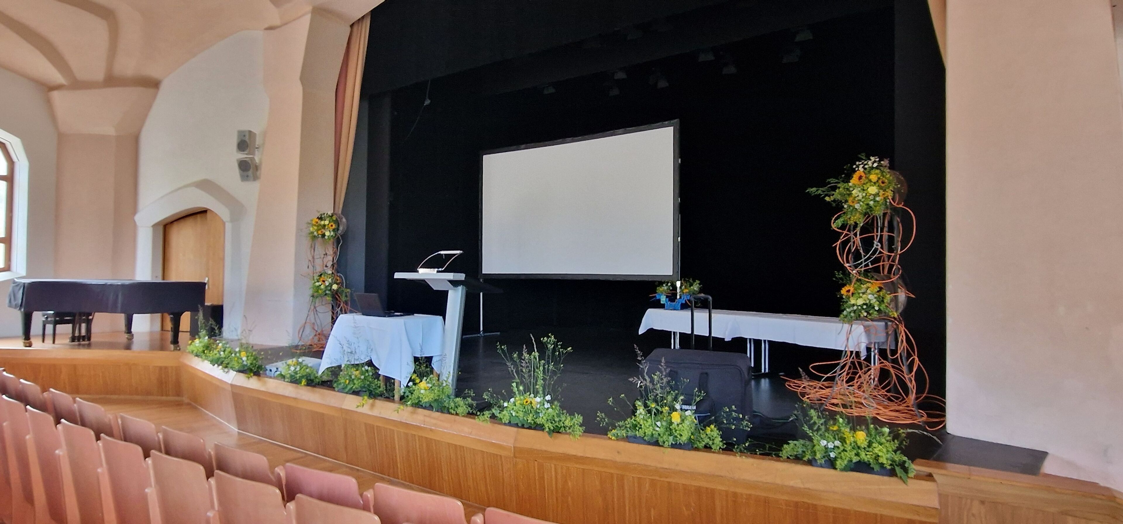 Un auditorio con un escenario, un piano y una pantalla de proyector.