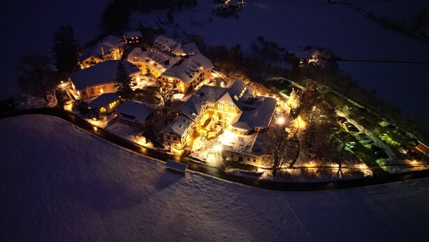 Un villaggio innevato di notte, con edifici illuminati e una strada tortuosa.