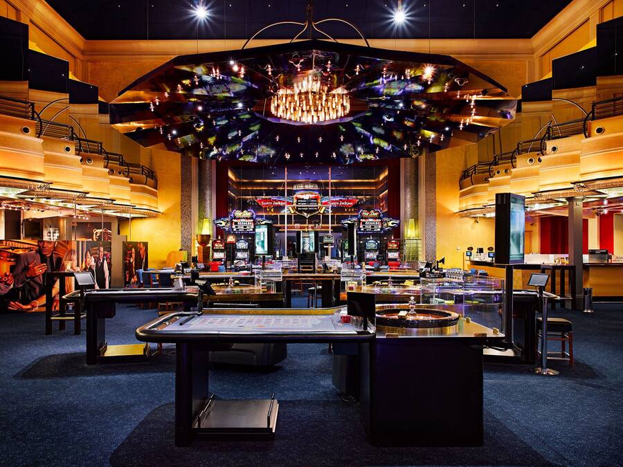 Un casino con varias mesas de blackjack, máquinas tragamonedas y una gran lámpara de cristal.