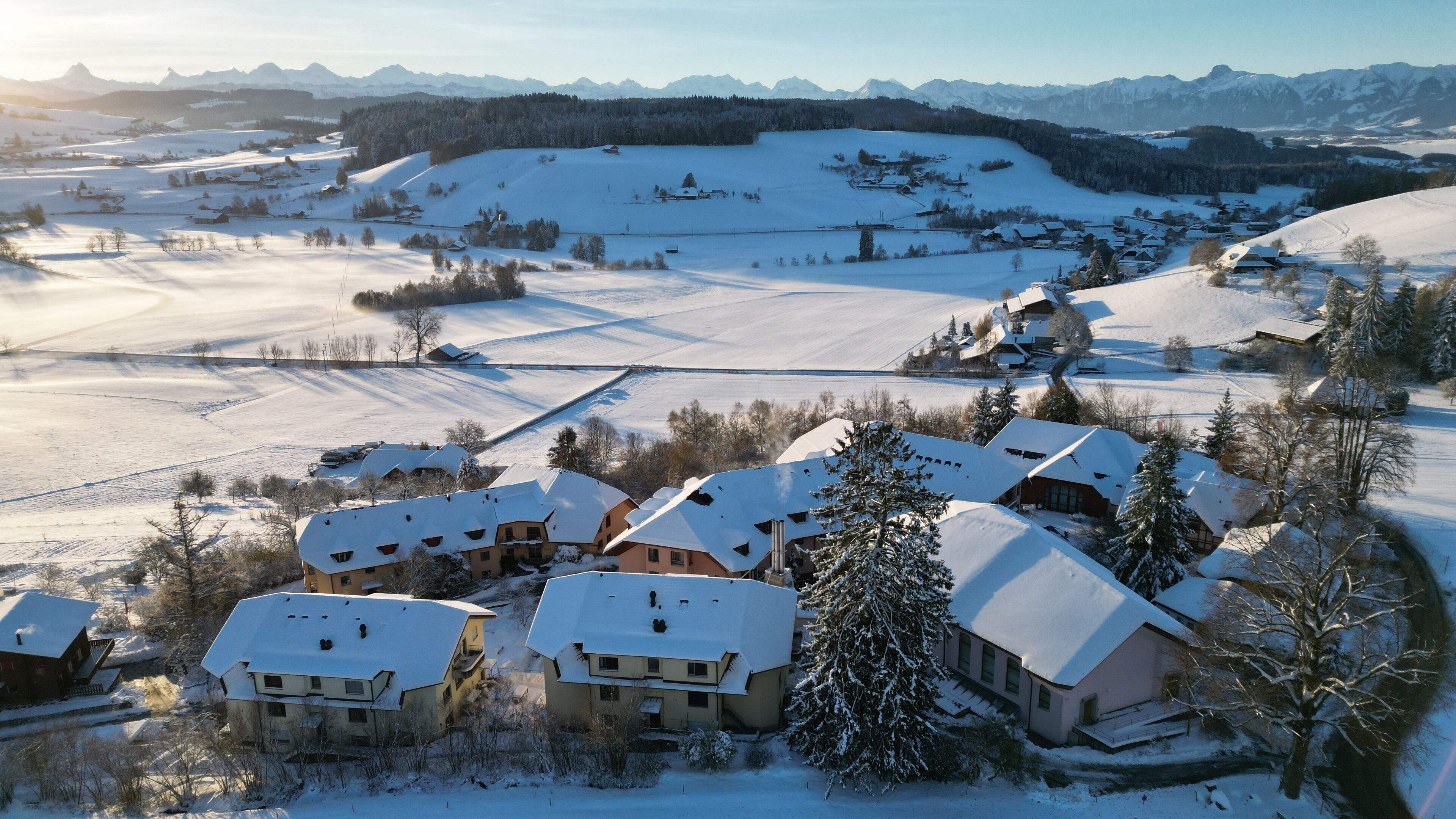 A snow-covered village with traditional houses, a ski slope, and a mountain range in the background.