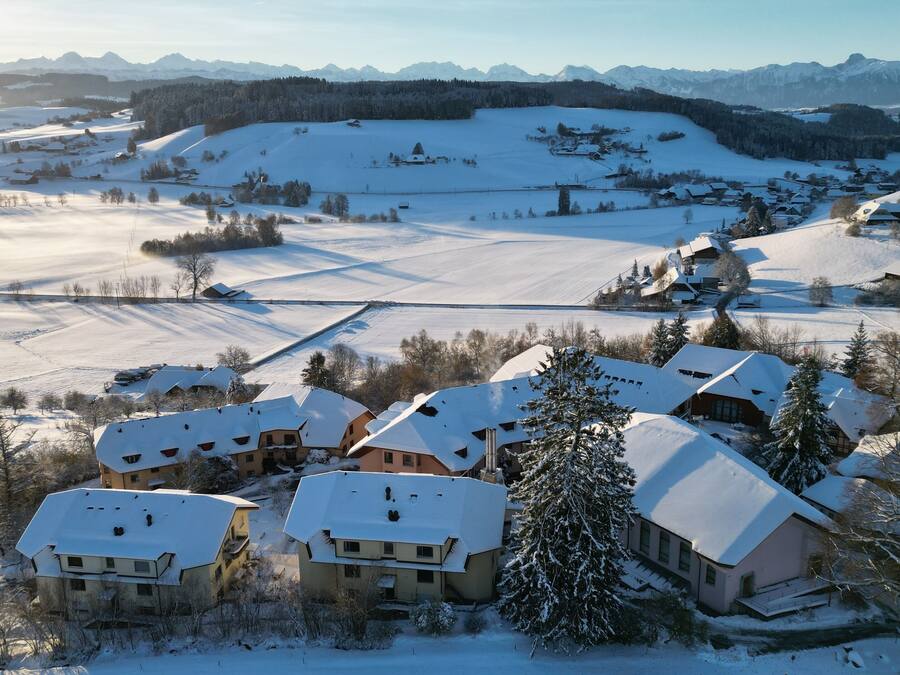 Een besneeuwd dorp met traditionele huizen, een piste en een bergketen op de achtergrond.