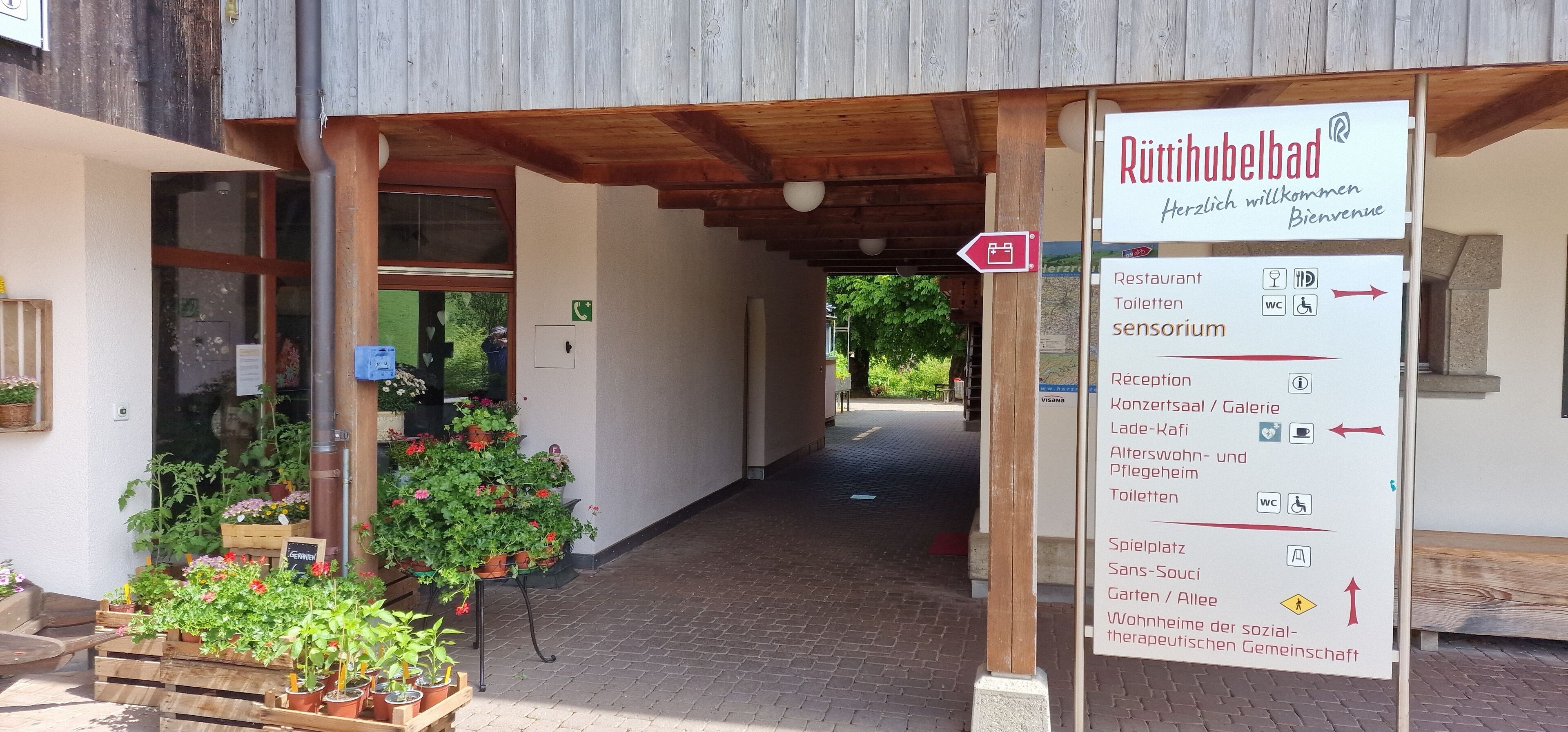 A wooden building entrance with a signboard indicating amenities such as a restaurant, toilets, and a reception area.