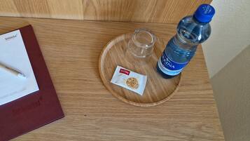 Una mesa de madera con un cuaderno rojo, un bolígrafo, un vaso, una botella de agua y un paquete de aperitivos.
