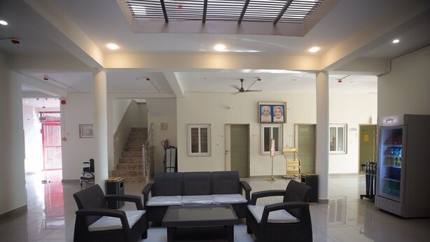 Un hall d’entrée spacieux avec un plafond haut, un espace de détente central avec des canapés et des fauteuils, un escalier et un distributeur automatique.