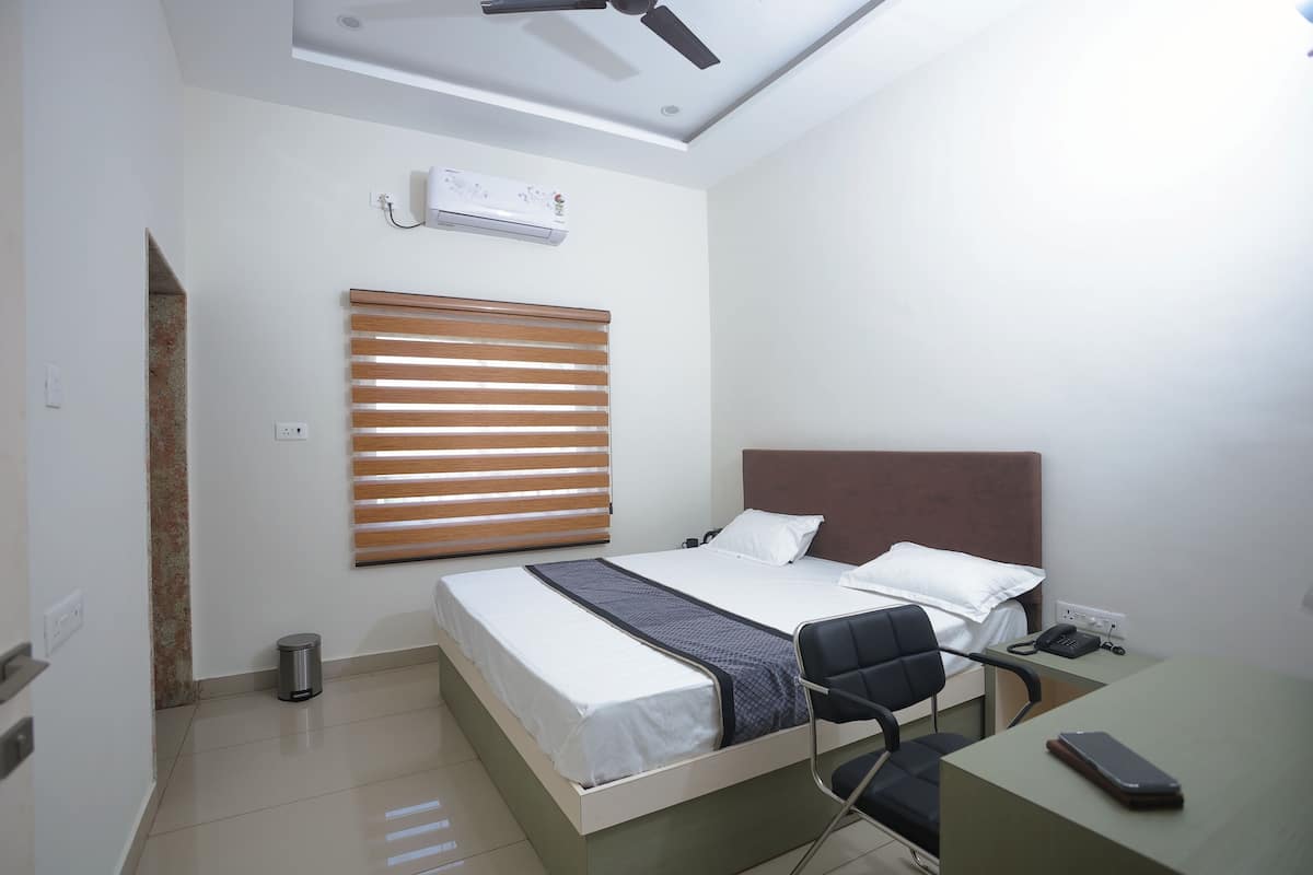 Habitación de hotel con cama, escritorio, silla, ventilador de techo, aire acondicionado y un cubo de basura.