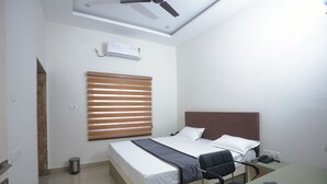 Une chambre d’hôtel équipée d’un lit, d’un bureau, d’une chaise, d’un ventilateur de plafond, d’un climatiseur et d’une poubelle.