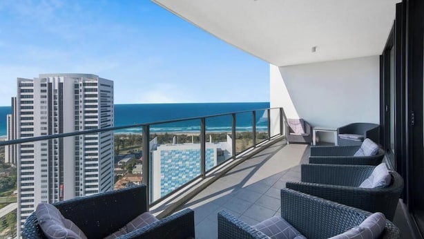 A balcony with wicker furniture, a glass railing, and a view of the ocean and buildings. - Sky Lounge 4BR Sub Penthouse (Gold Coast)