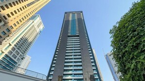 A tall, modern skyscraper with a glass facade, surrounded by other high-rise buildings. - Cosmos Living Delightful Studio (Dubai)
