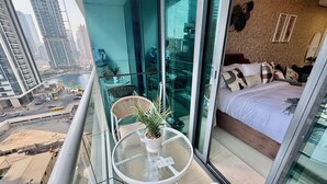 A balcony with a glass door, a round table with a potted plant, and a bed with pillows. - Cosmos Living Delightful Studio (Dubai)