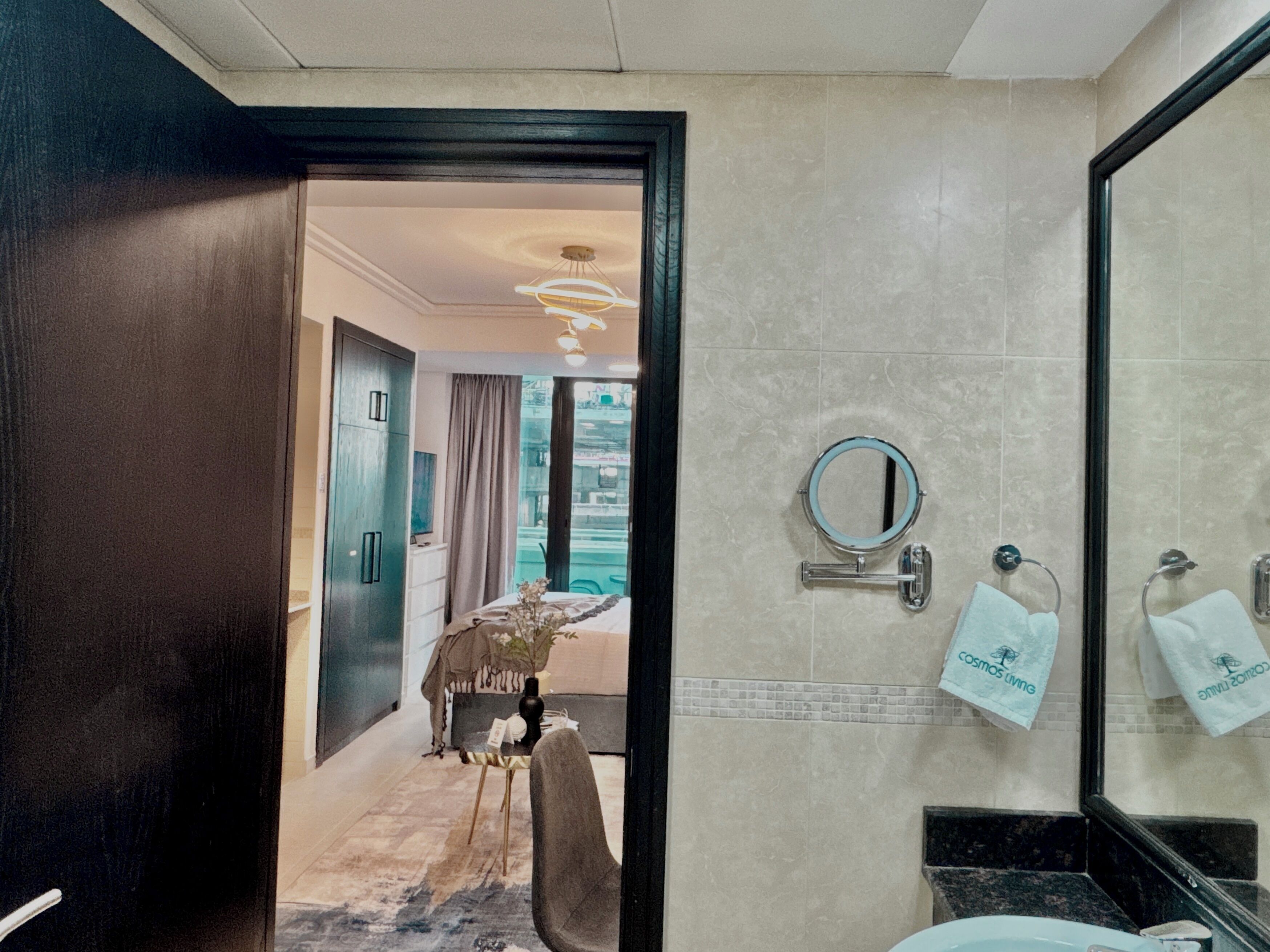 A hotel bathroom with a sink, mirror, towel rack, and a view of the hotel lobby.