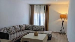 A living room with a sofa, a coffee table, a lamp, and a window with curtains.