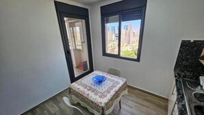 A small dining area with a table and chairs, a view of the city through a window, and a kitchen area with a sink.