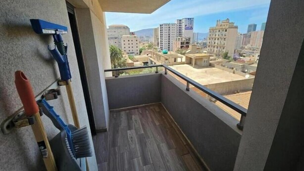 A balcony with a view of a cityscape, a wooden floor, and a wall-mounted shelf with cleaning supplies.