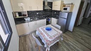 A compact kitchen with a dining table, white cabinets, a microwave, and a refrigerator.